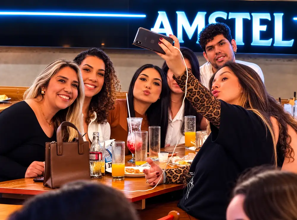 Grupo de amigos tirando selfie na mesa do Seu Barzin sob o letreiro Amstel